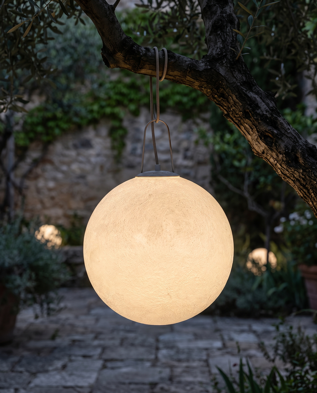 Outdoor moon lamp hanging from a tree in a courtyard at night