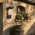 Black wall sconce on rustic stone cottage wall beside arched window with geraniums